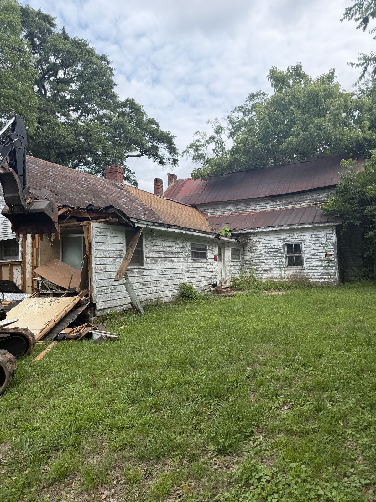 Old white farmhouse before demolition, excavator beginning to tear into the structure